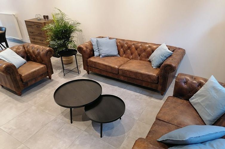 Gezellige zithoek in THE FRONT DOOR N28, vakantiehuis in Ieper, West-Vlaanderen, met leren banken en stijlvolle tafels.