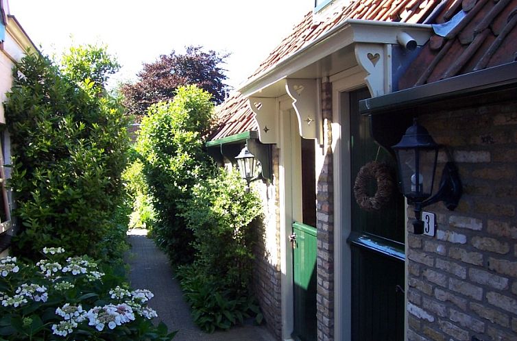Charmante ingang van Appartement De Kwikstaart in Den Burg, Texel, omgeven door weelderige natuur en rustieke stenen muren.