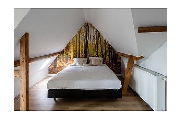 Sfeervolle slaapkamer in Boeckhaege vakantiehuis, Ronse, Oost-Vlaanderen, met rustiek houten balken en bosprint op de muur.