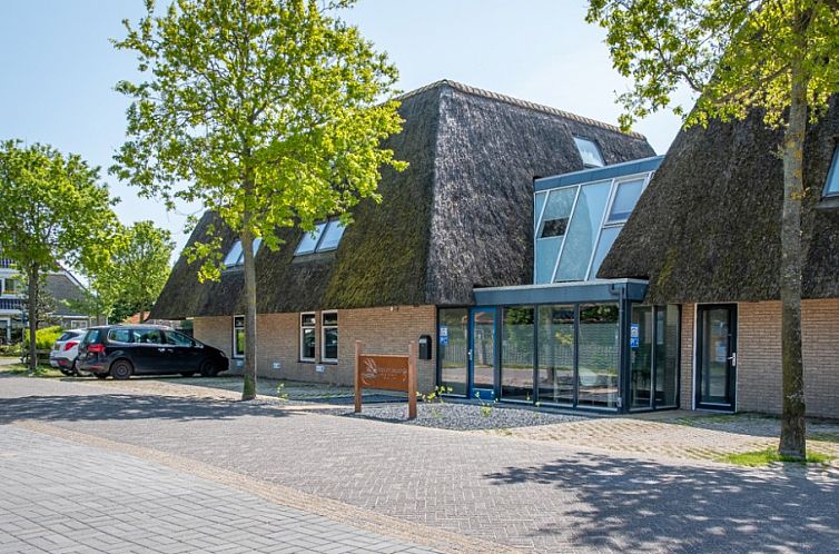 Vooraanzicht van Waddenresidentie Ameland vakantieappartement in Buren, Waddeneilanden, met rieten dak en groene omgeving.