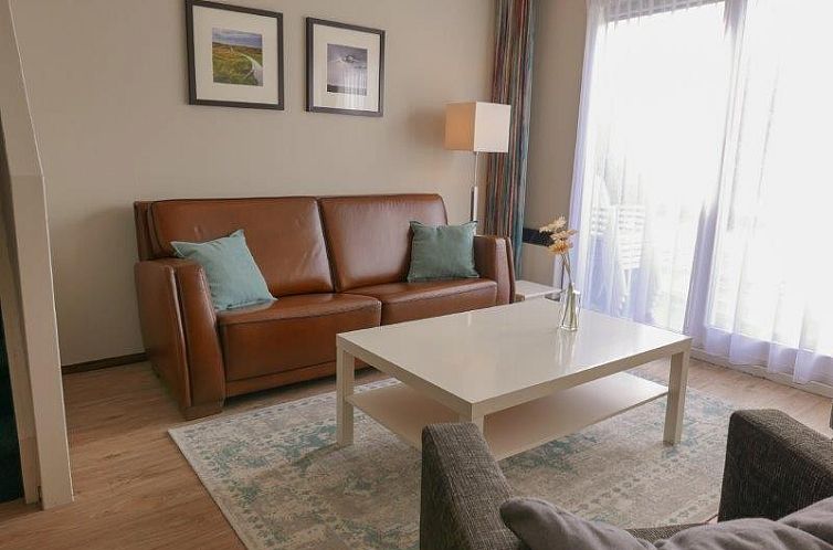 Gezellige woonkamer in Appartement Amelander Kaap 2, Hollum, Ameland met comfortabele bank en veel daglicht.