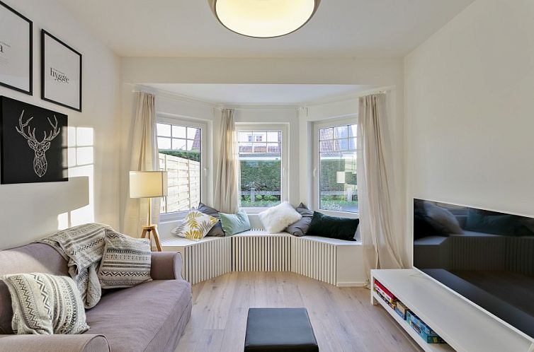 Gemuetliches Wohnzimmer in Maison Lucie, einem Ferienhaus in Koksijde an der belgischen Kueste, mit bequemer Sitzecke und grossen Fenstern.