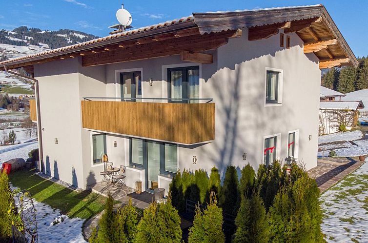 Rustikales Ferienhaus Ferienwohnung Krimbacher in Brixen im Thale, Tirol, umgeben von Schnee und Bergen, mit einem einladenden Balkon.