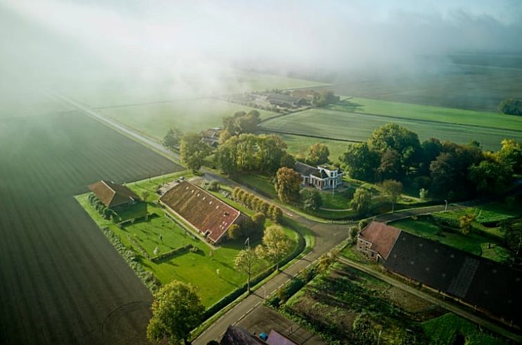 Luchtfoto van Vakantiehuis in Nieuwolda, Noordoost Groningen, omgeven door weelderige natuur en uitgestrekte velden.